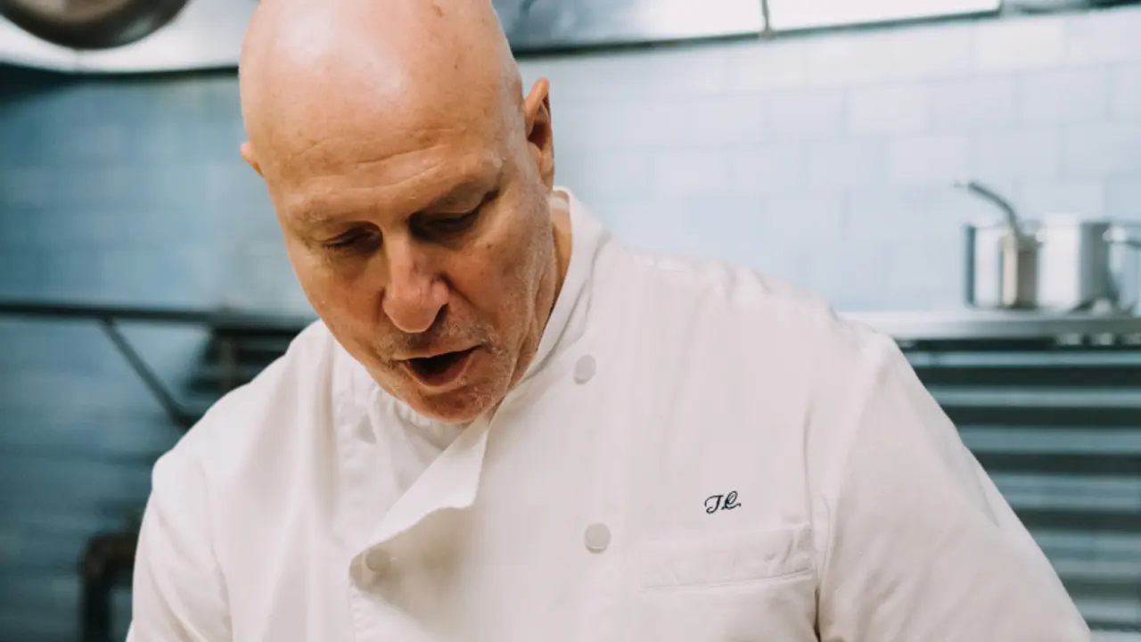 A focused chef in a white jacket is concentrating on preparing food in a professional kitchen setting.