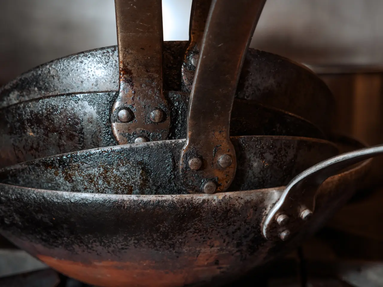 Stacked weathered cast iron skillets showing their handles and rivets.