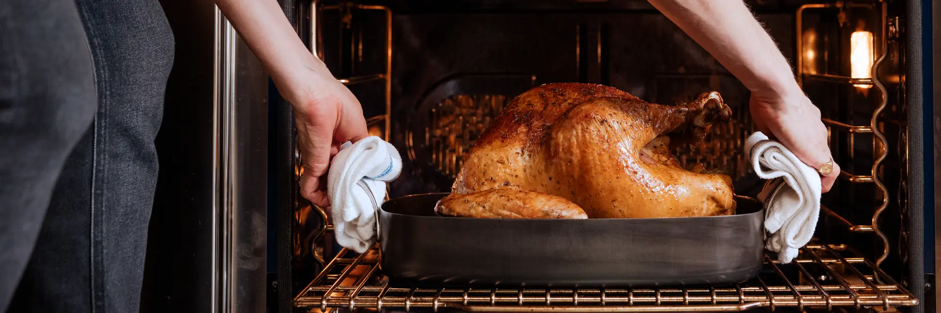 A person is taking a golden-brown roasted turkey out of the oven using oven mitts.