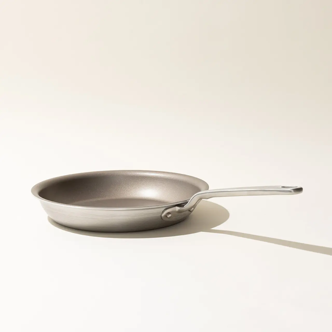 A frying pan with a metal handle on a plain background, casting a soft shadow to the right.
