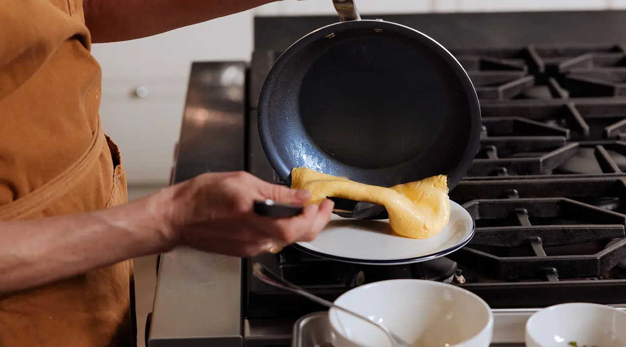 A person is flipping a crepe in a kitchen setting using a non-stick frying pan.
