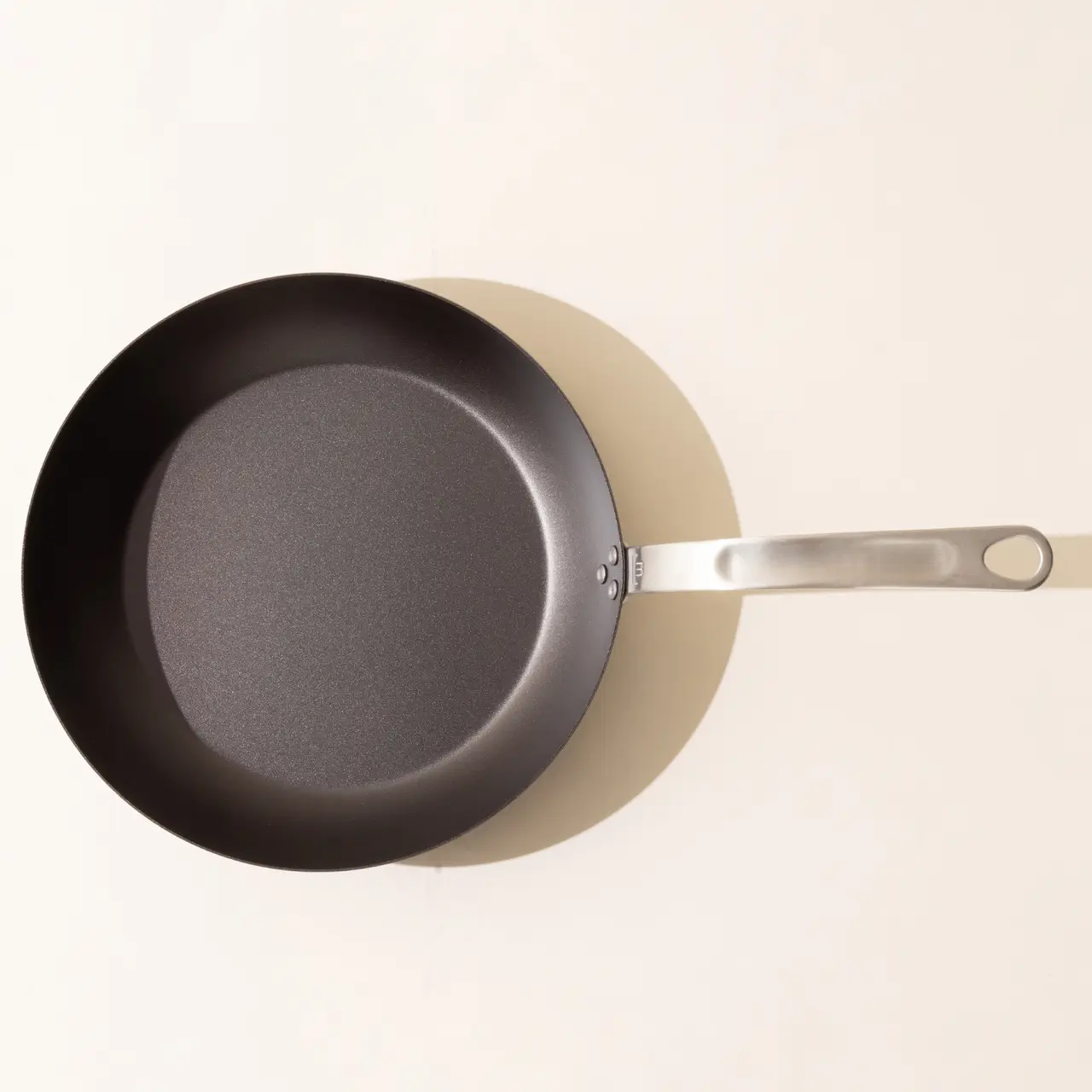 A new non-stick frying pan with a stainless steel handle positioned on a beige surface.