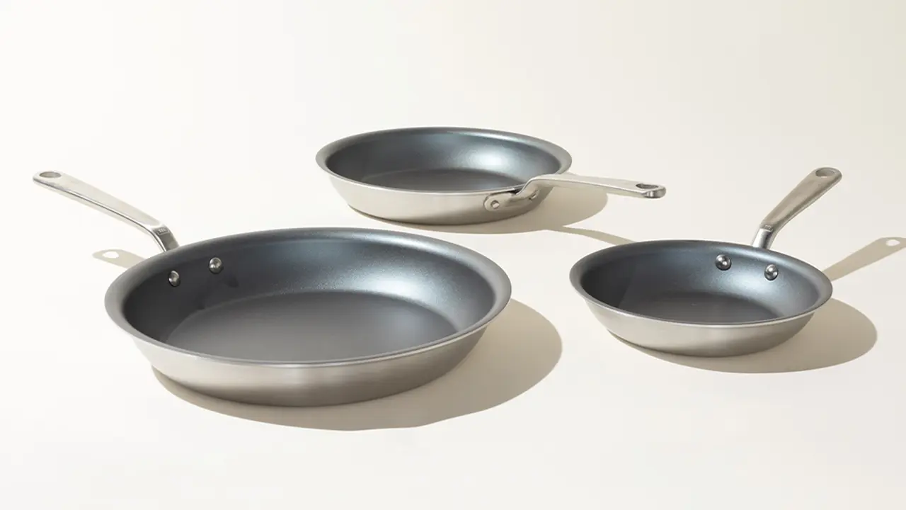 Three different-sized non-stick frying pans with silver handles are displayed against a plain background.