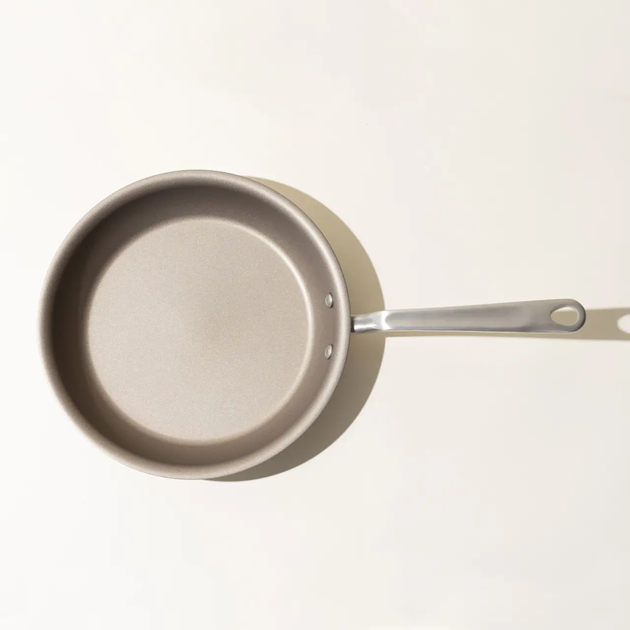 A non-stick frying pan with a silver handle, viewed from above on a light background.