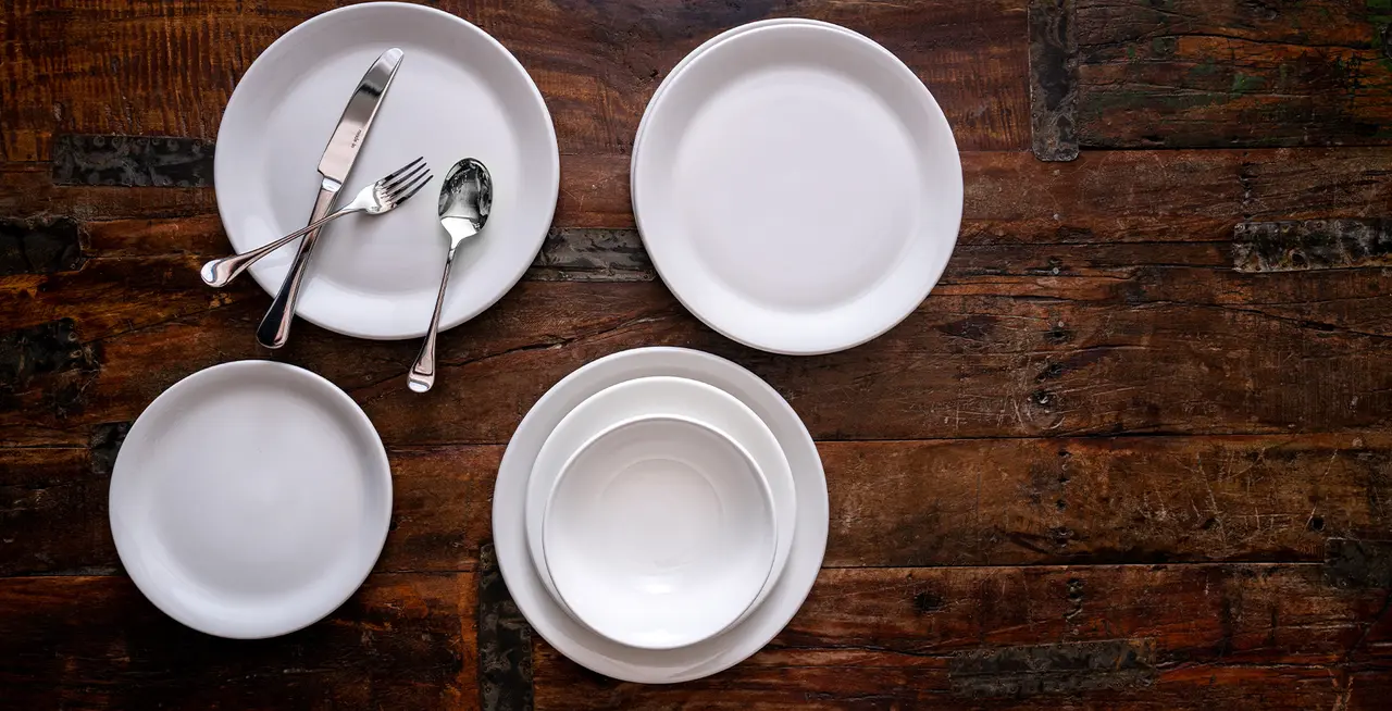A set of empty white dishes and silverware arranged neatly on a dark wooden table.