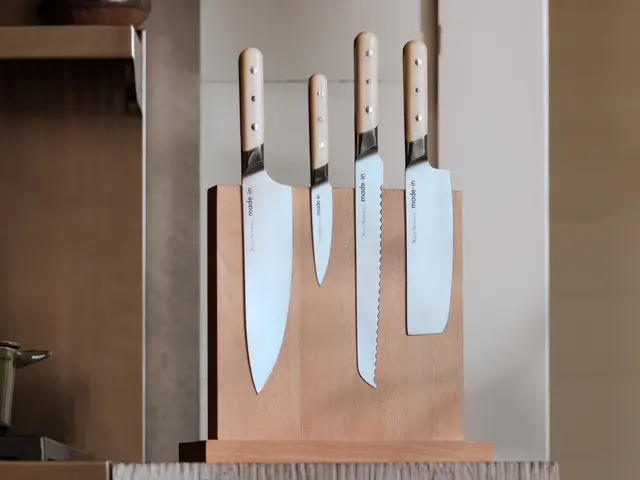 A set of four kitchen knives with light-colored handles are neatly placed in a wooden knife block on a countertop.
