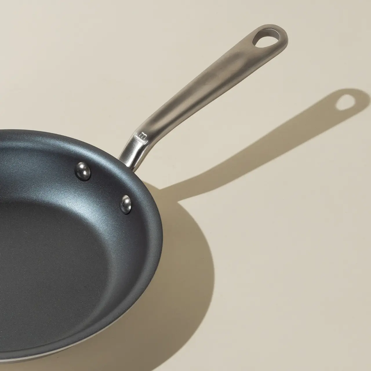 A frying pan casts a shadow on a light surface, illustrating its form and handle.