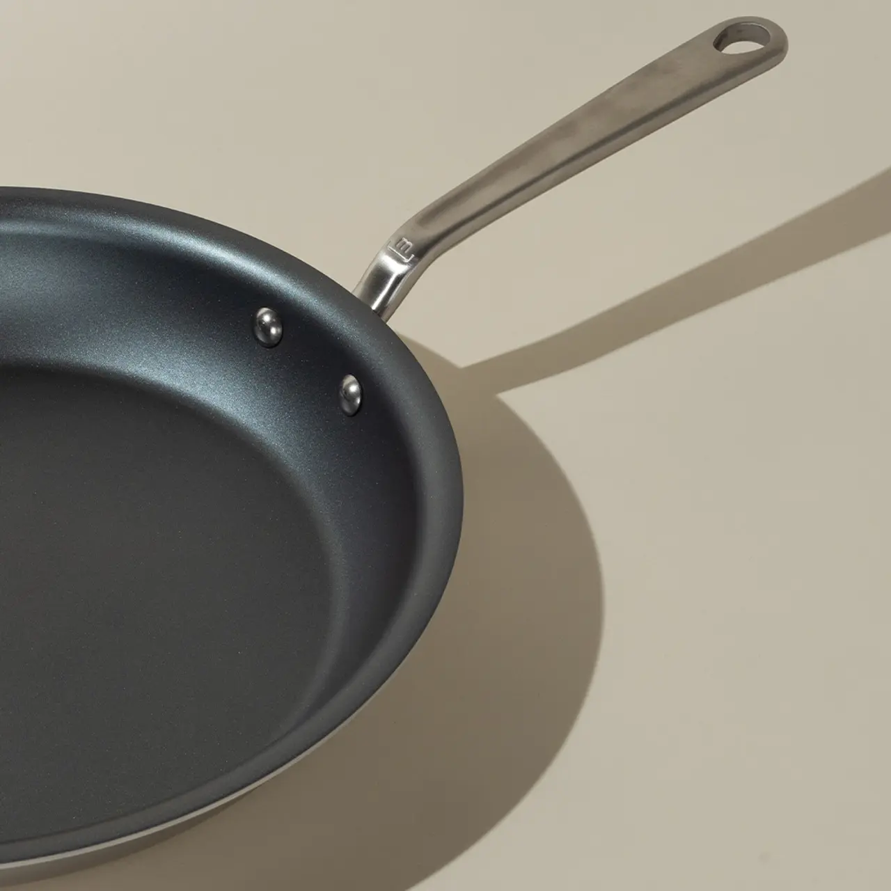 A non-stick frying pan with a stainless steel handle is presented against a neutral background, casting a soft shadow.