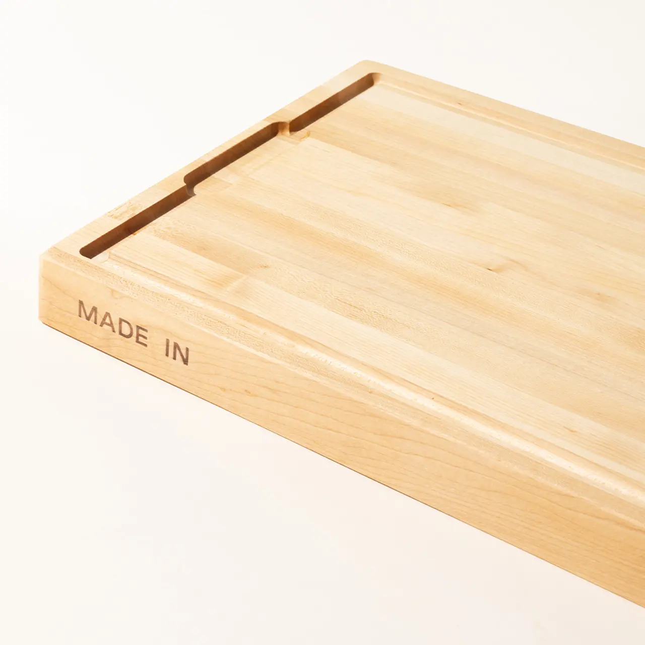 A close-up of a wooden cutting board with a juice groove and the words "MADE IN" stamped on the side.