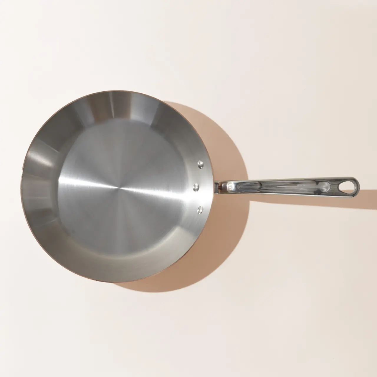 A stainless steel frying pan with a long handle is shown from above against a neutral background.