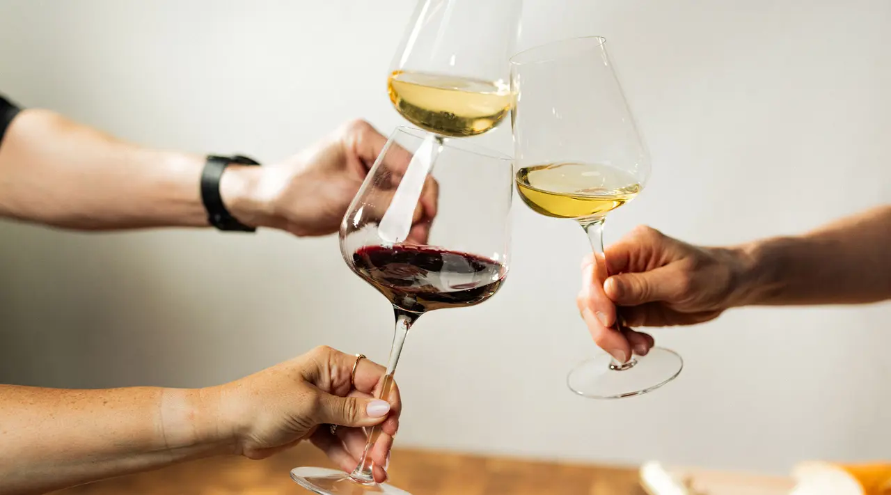 Three people are clinking glasses of red and white wine together in a toast.