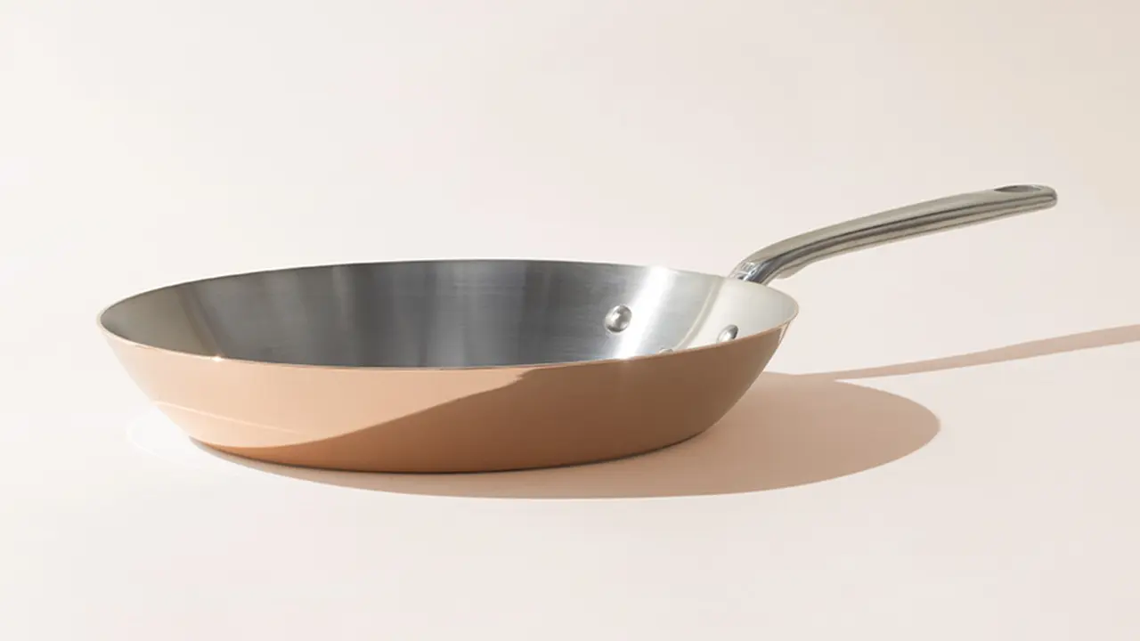 An empty stainless steel frying pan with a silver handle is set against a light background, casting a slight shadow to the right.