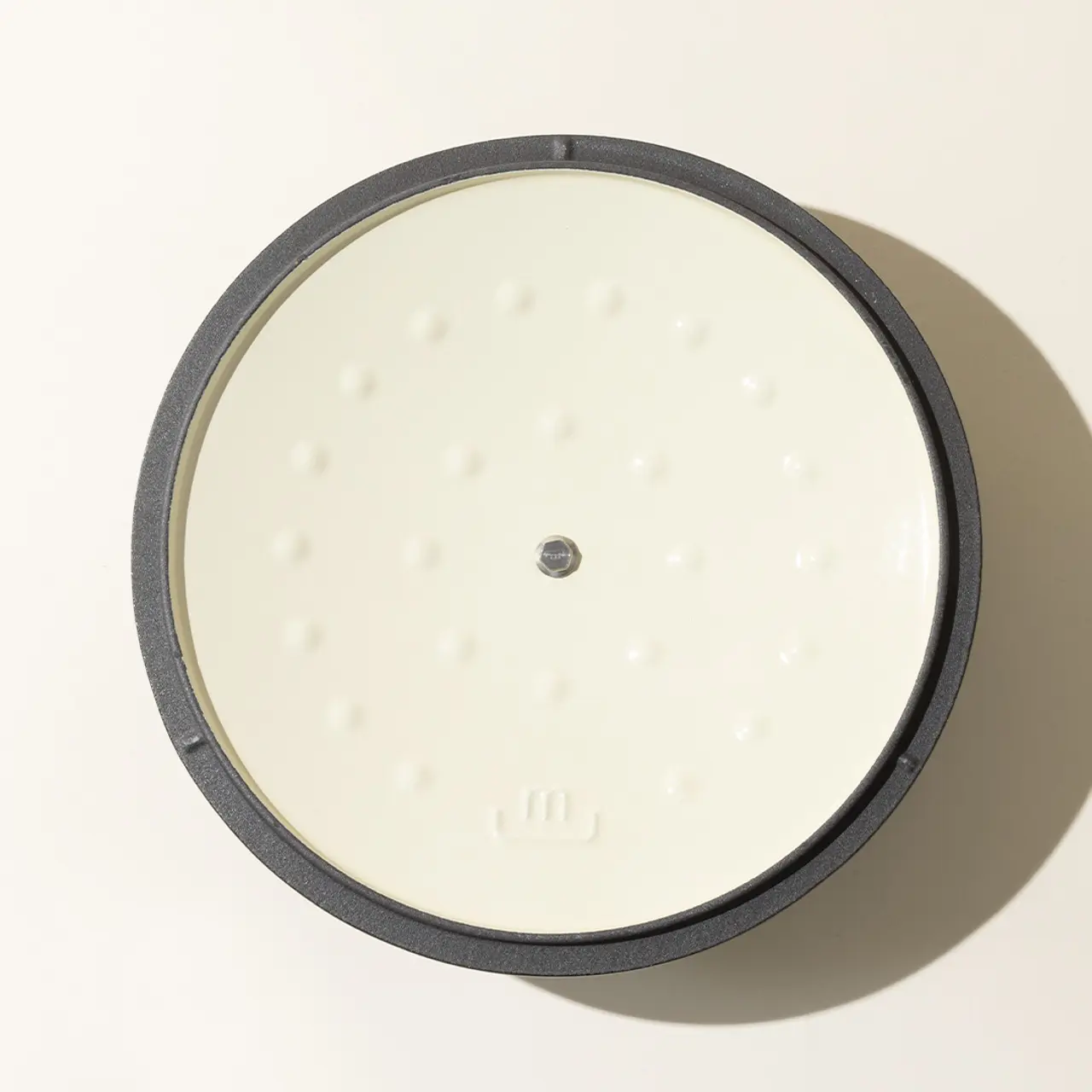A top-down view of a white, round, braille-labeled device with a single, centered button and a dark border.