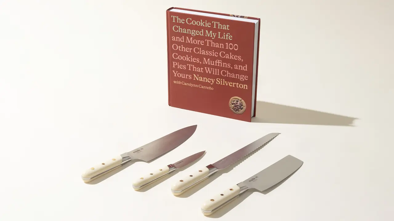 A row of four kitchen knives with white handles lies in front of a red cookbook titled "The Cookie That Changed My Life" by Nancy Silverton.
