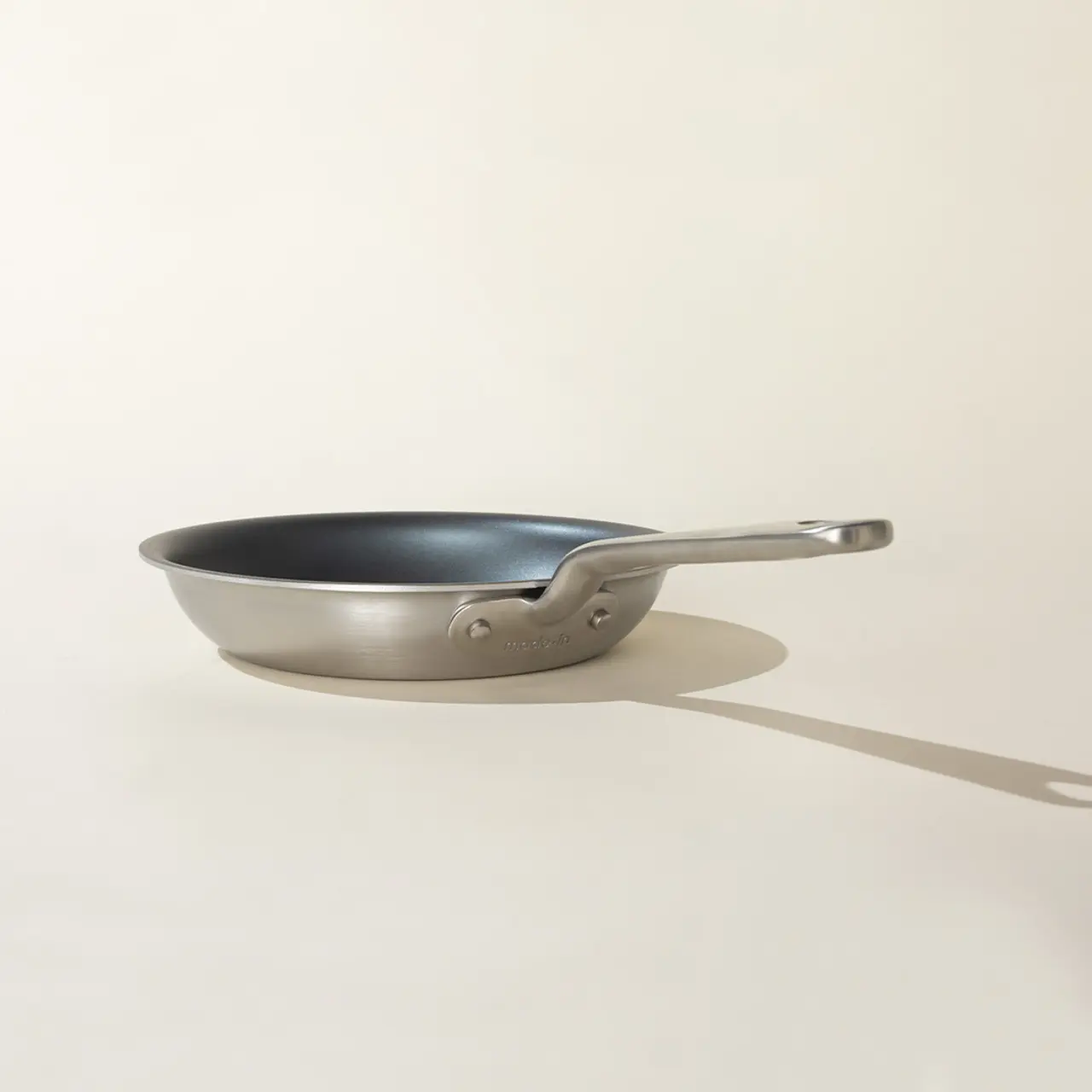 A stainless steel frying pan casts a long shadow on a light background.