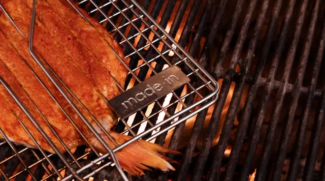 A piece of fish is being grilled on a barbecue rack with a "made in" label visible.
