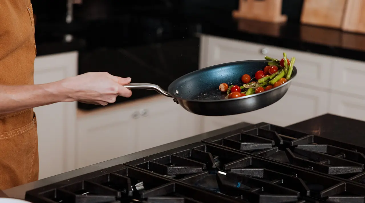 A person is tossing vegetables in a frying pan over a stove.