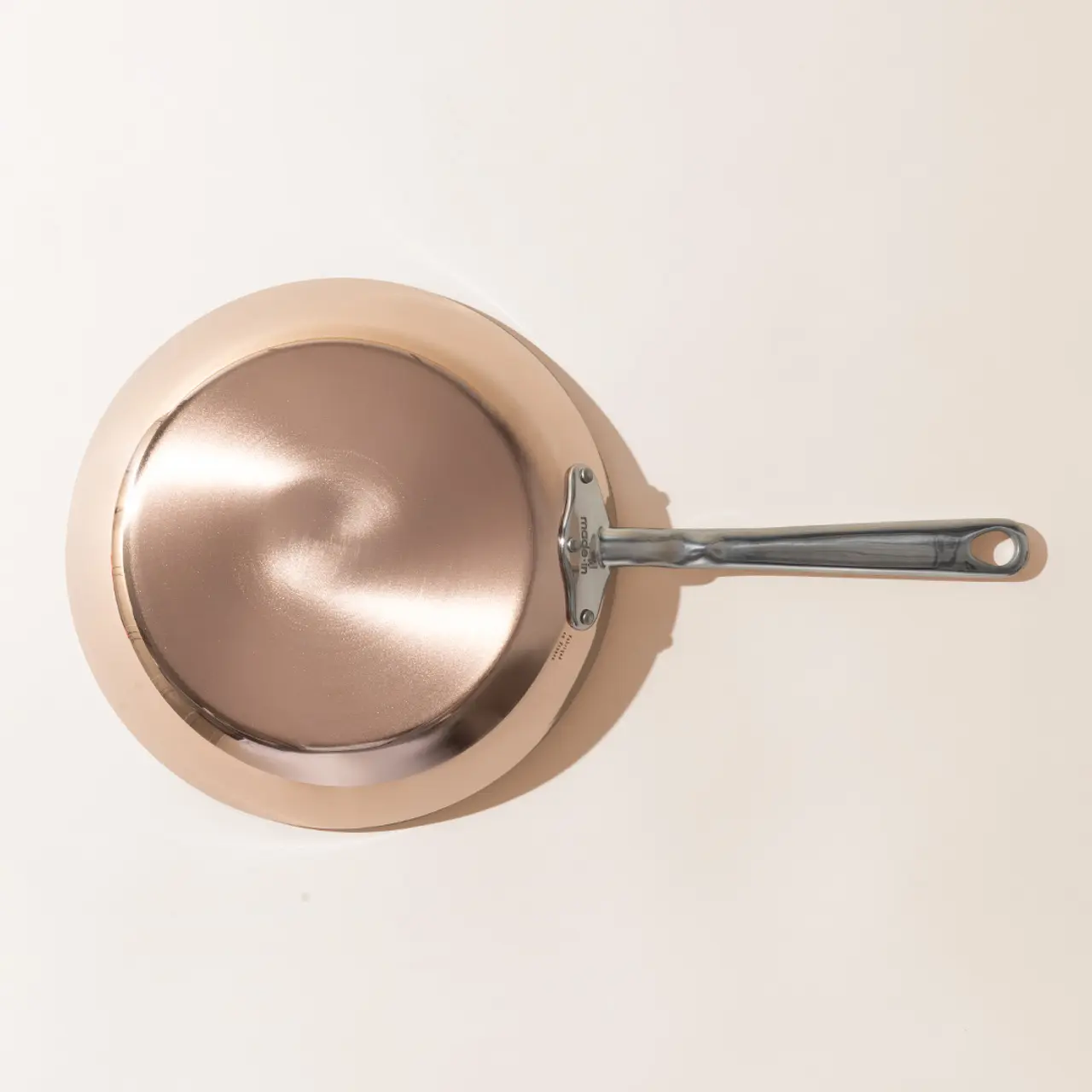 A top-down view of a new copper-colored frying pan with a stainless steel handle on a light background.