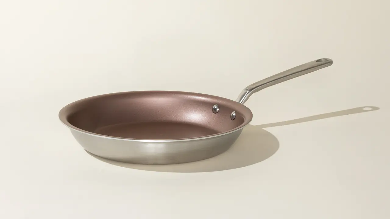 A non-stick frying pan with a stainless steel handle is positioned against a neutral background.