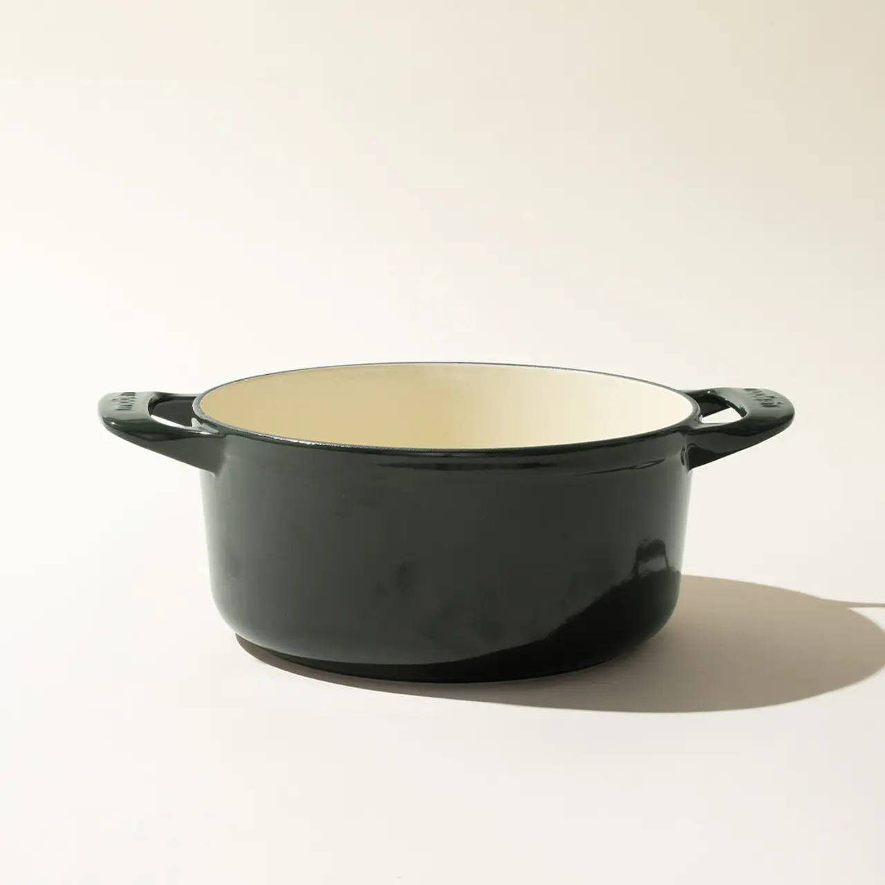 A simple dark-colored cooking pot with two handles placed against a light background.