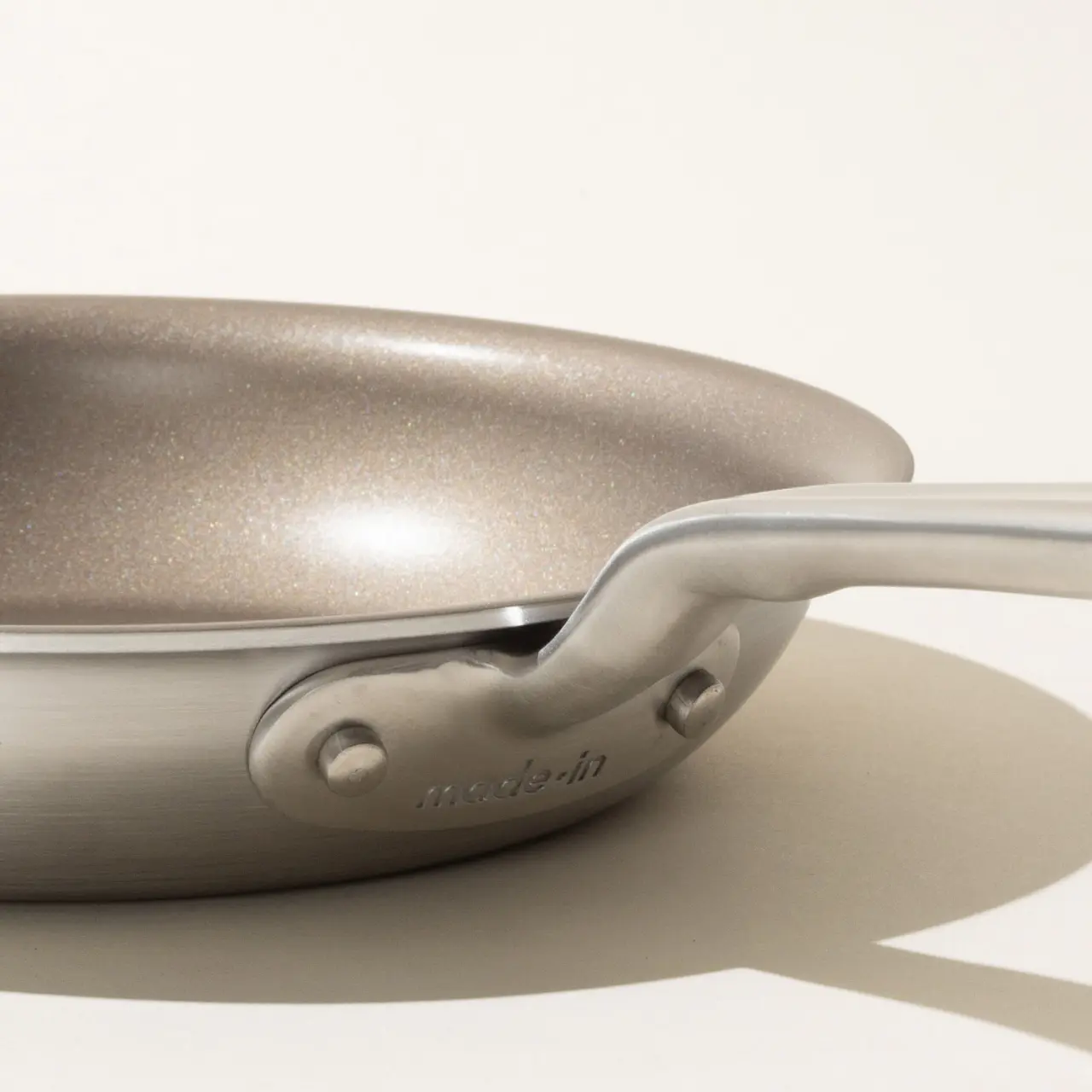 Close-up side view of a modern frying pan with a silver handle on a light background.