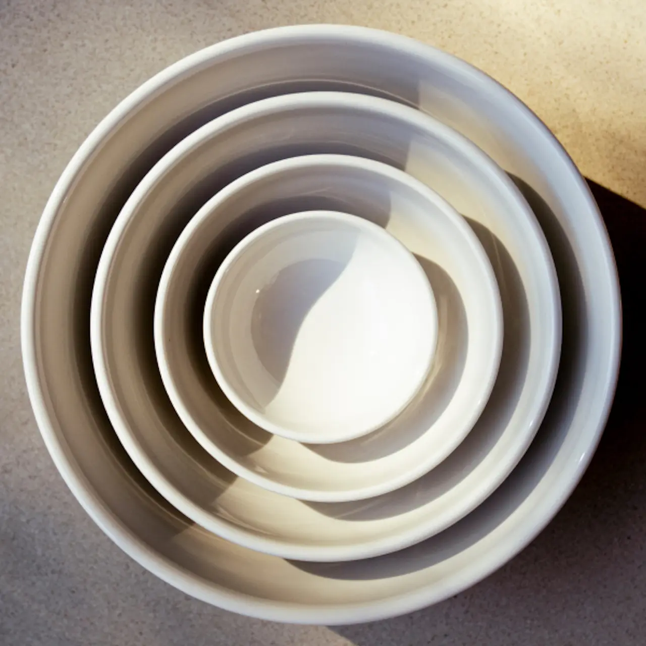 A top-down view of a set of nested white mixing bowls on a surface, creating a gradation of sizes from large to small.