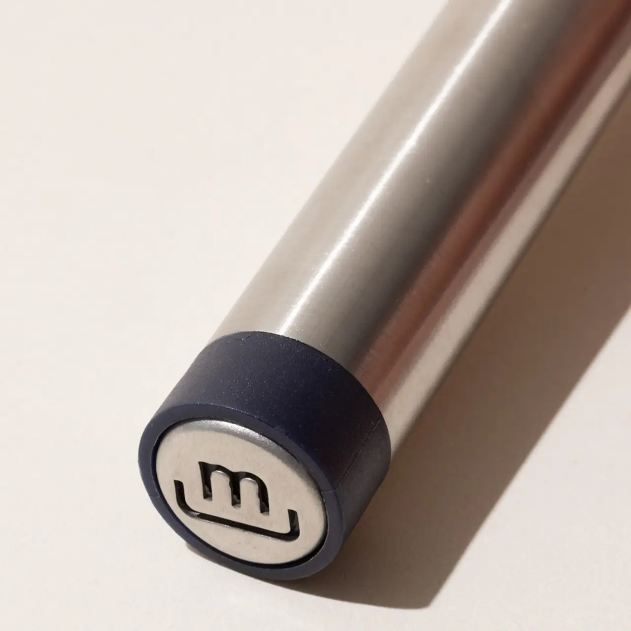 A close-up of a cylindrical metallic object with an end cap featuring a logo with the letter "M" embossed on it.