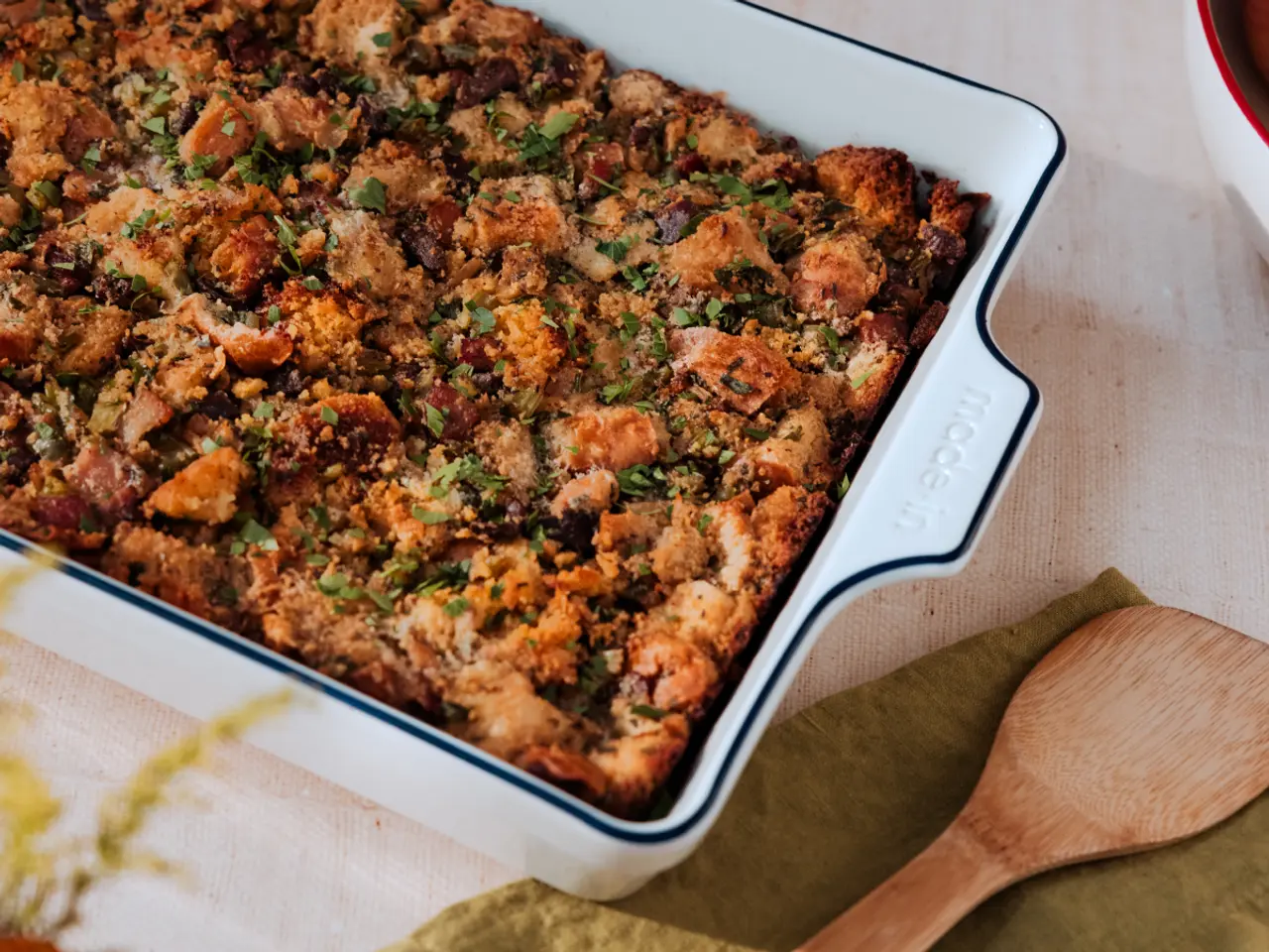 A freshly baked casserole with a golden-brown crust sprinkled with herbs is presented in a white baking dish next to a wooden spatula.