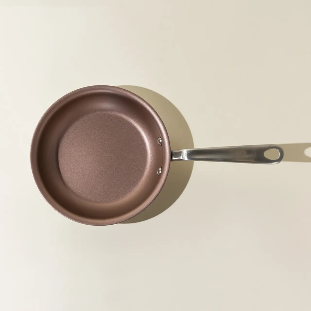 A brown non-stick frying pan with a silver handle is shown from a top-down perspective.
