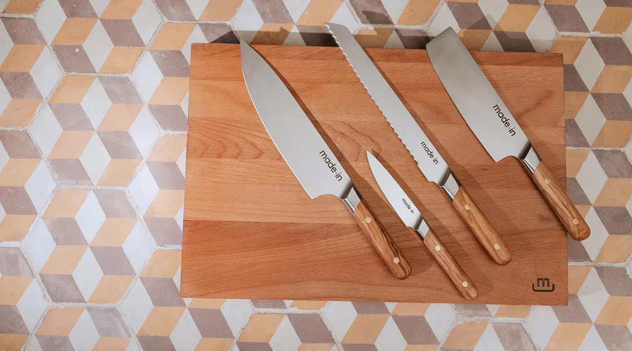 Three different-sized kitchen knives with wooden handles are neatly placed on a wooden cutting board over a tiled countertop.