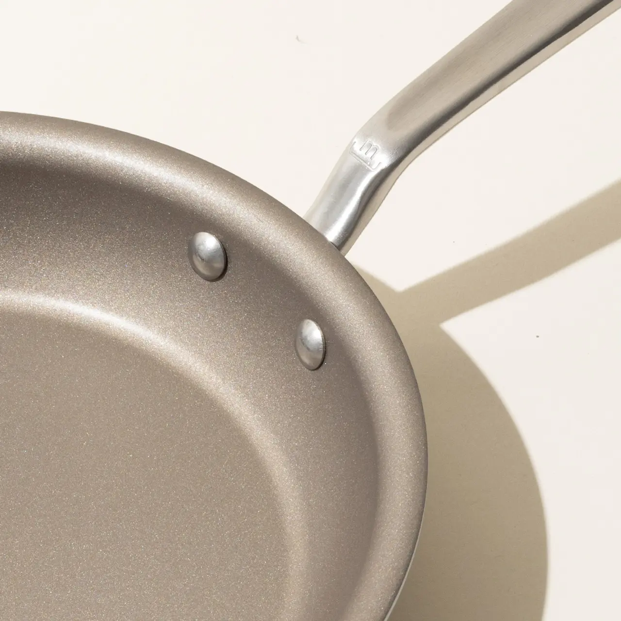 A close-up of a non-stick frying pan with a metallic handle, casting a shadow on a light surface.