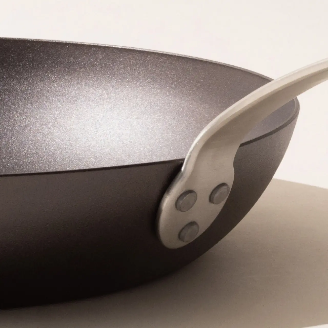 A close-up of a black frying pan with a silver handle, set against a neutral background.