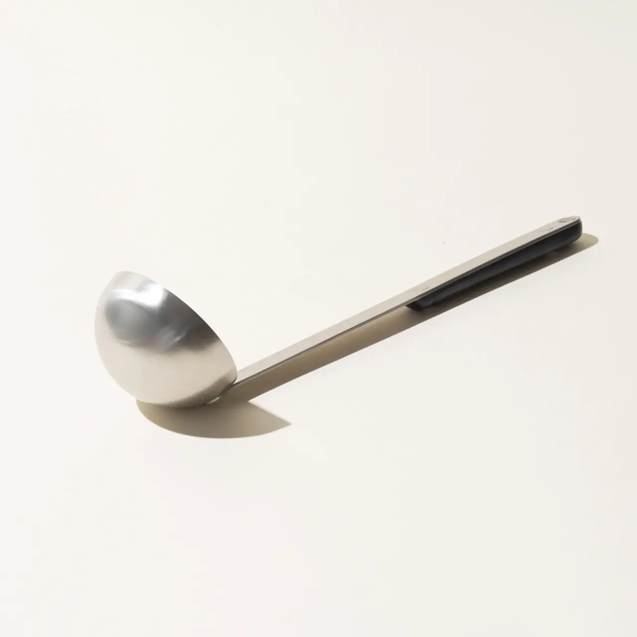 A single stainless steel spoon is centered on a plain light background, lying with the bowl facing up.