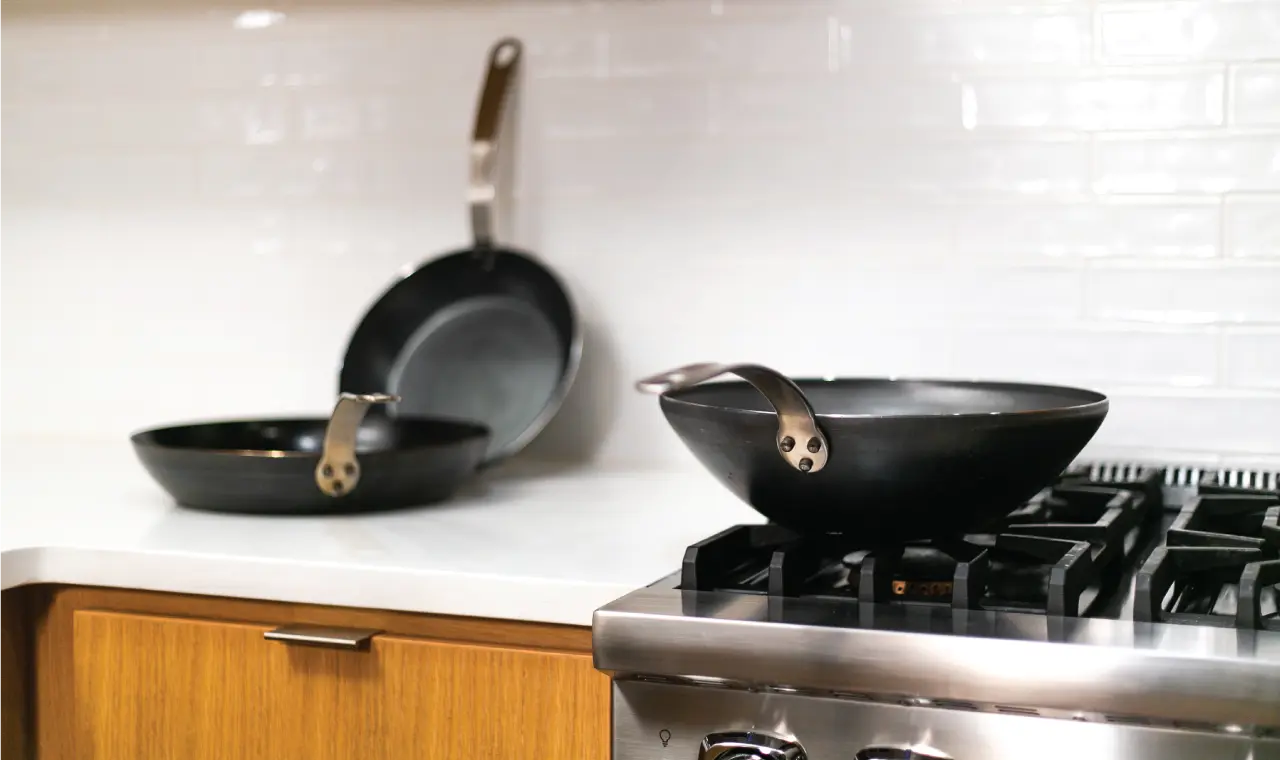Two black frying pans on a modern stovetop in a kitchen with white subway tile backsplash and wooden cabinetry.